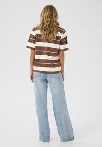 Chemise à manches courtes rayée marron et crème avec une coupe ample, associée à un jean large bleu clair. Design simple, en matériau coton.