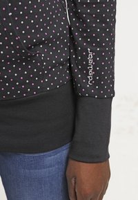 Sudadera negra con lunares púrpuras y grises, con un bolsillo tipo canguro y puños de canalé. Logo "Nad fashion" bordado en plata.