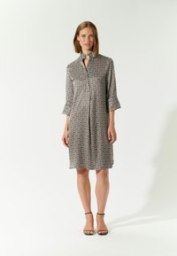 Abito camicia in tessuto testurizzato con motivo geometrico in tonalità di nero e crema. Presenta un colletto e maniche a tre quarti.