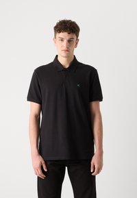 Zwarte polo in gestructureerde stof, met een driedelige knopenlijst en een groene CK-logo op de linkerkant van de borst. Korte mouwen, klassieke pasvorm.