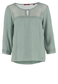 Blusa verde chiaro con maniche lunghe, tessuto testurizzato e scollatura in rete. Presenta un collo a chiave e cuciture decorative sui polsini.