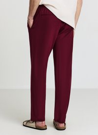 Pantaloni leggeri color bordeaux con vita elastica, tasche laterali e design a gamba dritta; abbinati a sandali chiari.