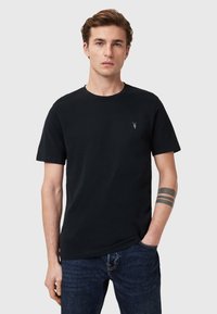 Musta puuvillapaita pyöreällä pääntiellä, lyhyet hihat ja pieni kirjailtu logo rinnassa; yhdistetty tummiin farkkuihin.