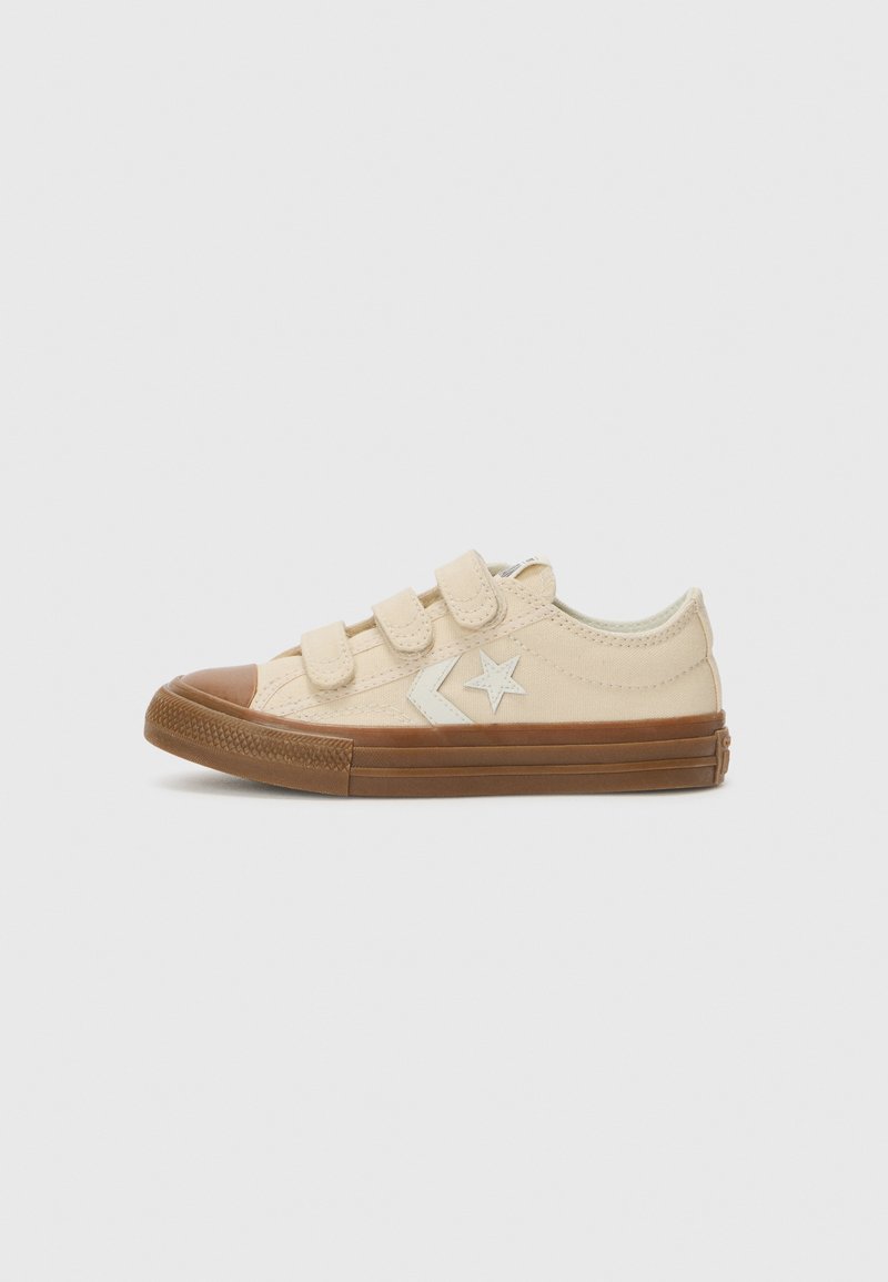 Μπεζ καμβάδες αθλητικά παπούτσια με τρεις ρυθμιζόμενες ταινίες Velcro, καφέ καπάκι από καουτσούκ στη μύτη και υφασμάτινη σόλα. Λευκό αστέρι και βέλος για διακόσμηση στο πλάι.