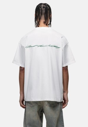 T-shirt bianco in cotone con scritta cursiva verde "Good For Nothing" sul retro. Vestibilità rilassata con maniche corte, texture liscia e senza ulteriori dettagli.