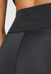 Leggings de sport noirs avec une taille haute, une texture de tissu lisse, des coutures contrastées et un discret logo.