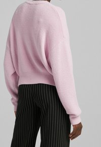 Pull rose pâle et moelleux avec épaules tombantes et ourlet côtelé, associé à un pantalon noir à fines rayures. Texture douce, coupe décontractée.