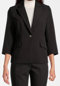 Černý blazer s jedním knoflíkem, klopami a dvěma předními našitými kapsami. Má rukávy tříčtvrteční délky a hladký povrch.