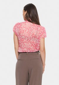 Pink floral blouse with short puff sleeves and a soft, sheer fabric, paired with light brown dress trousers featuring back pockets.