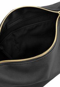 Borsa a pochette in pelle nera con una cerniera dorata, caratterizzata da una consistenza morbida e una singola tasca interna in tessuto nero. Etichetta FREDsBRUDER visibile.