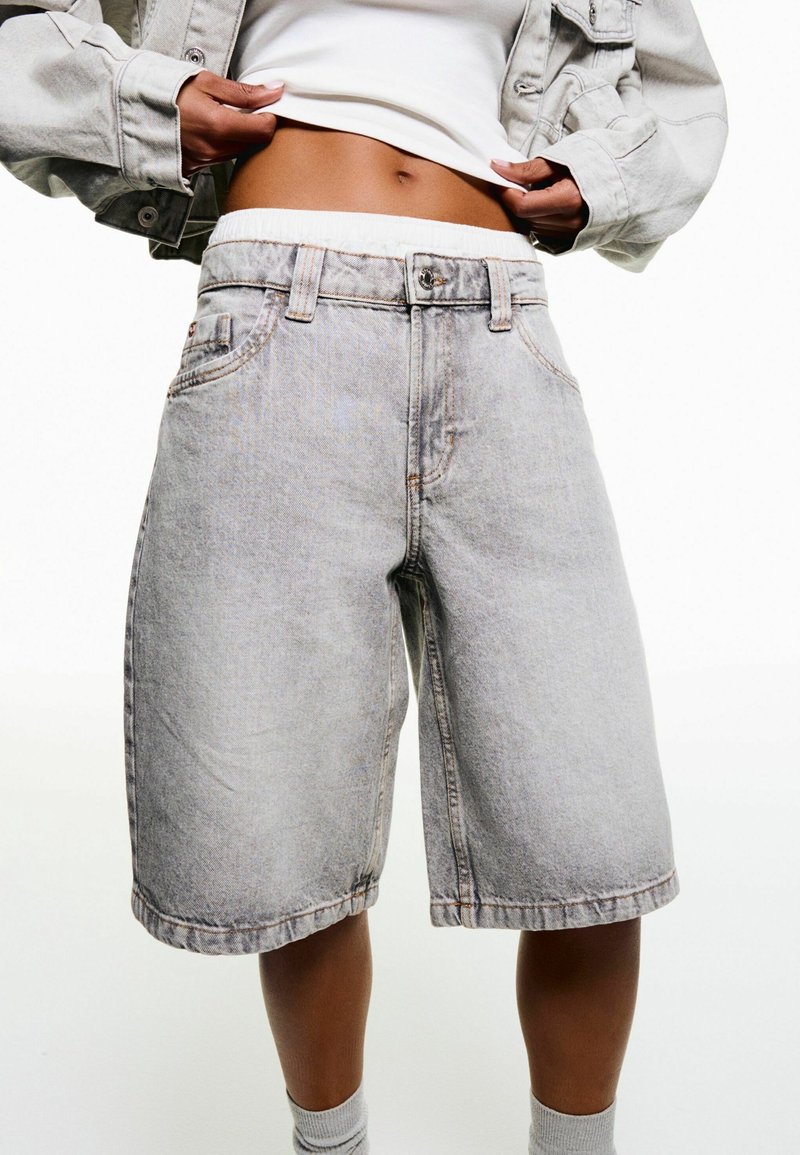 Shorts in denim grigio chiaro con vestibilità comoda, caratterizzati da una vita con elastico e passanti per cintura, e dettagli cuciti sottili sui bordi.