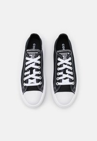 Baskets en toile noire avec lacets blancs et semelles en caoutchouc. Présentent des coutures blanches et un design classique. Marque Converse sur la languette.