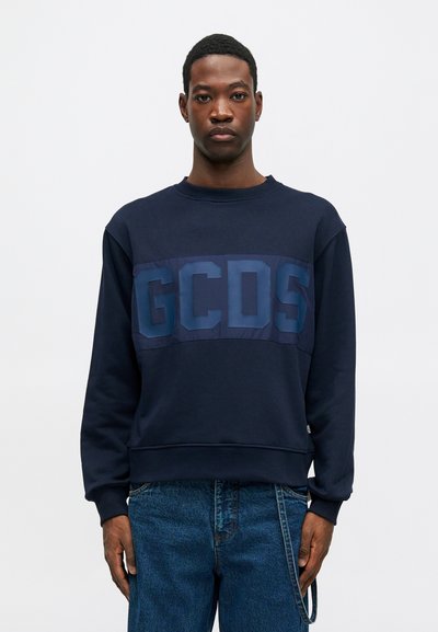 Marinblå sweatshirt med rund halsringning och långa ärmar som har en framträdande mörkblå "GCDS"-logotyp över bröstet. Blandning av bomull.