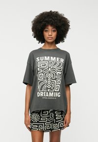 T-shirt gris surdimensionné avec un design graphique blanc portant le texte "SUMMER DREAMING". Associé à un short noir affichant un motif abstrait blanc.