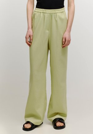 Pantalons large vert clair en tissu doux avec une taille élastique et deux poches latérales, associés à des sandales plates noires.