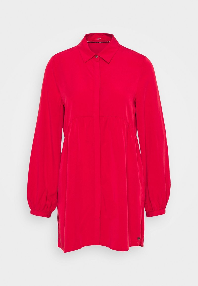 Blouse rouge vif à manches longues, col pointu, boutonnée devant, à coupe ample, présentée sur un fond blanc uni.