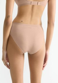 Beige hochgeschnittene Unterwäsche aus glattem Stoff, mit nahtlosem Design und einem dezenten Logo auf der Rückseite.