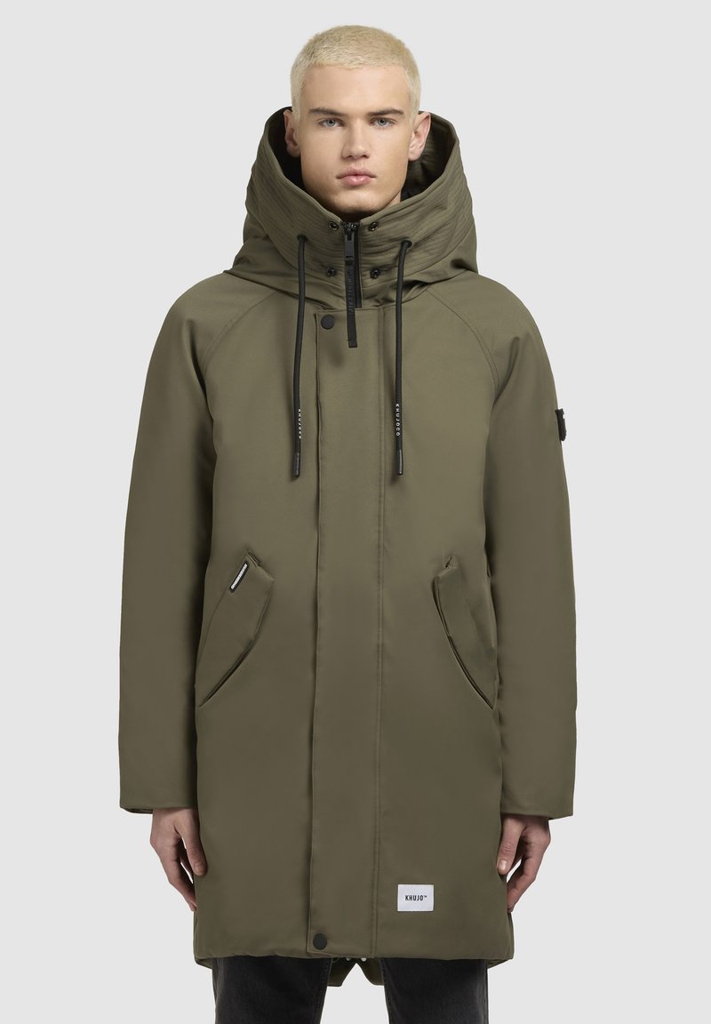 Olivengrøn parka-jakke med høj krave, justerbar hætte, forlommer og lynlåslukning. Har sorte snore og logo-patch.