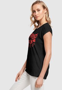 Schwarzes T-Shirt mit Rundhalsausschnitt und kurzen Ärmeln. Bedruckt mit rotem Grafiktext "FRIENDS" und einer Handillustration, aus Baumwolle gefertigt.