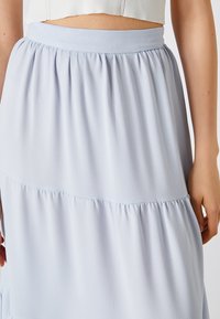 Jupe bleu clair à volants en tissu fluide. Elle présente une large ceinture élastique et une texture subtile avec des détails froncés aux coutures.