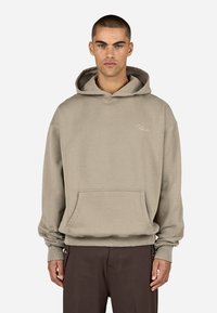 Jasne beżowe klasyczne hoodie z kieszenią z przodu, ściągaczami w mankietach i małym haftowanym logo na klatce piersiowej. Miękka, teksturowana tkanina.