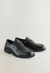 Schwarze Lederne Loafers mit glatter Oberfläche, ausgestattet mit einem Riemen über dem Spann, runder Zehenform und einem niedrigen gestuften Absatz.