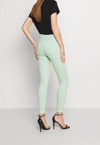 Mentolově zelené skinny džíny s vysokým pasem, s kapsami na zadní straně, v kombinaci s černým tričkem a černými sandály na vysokém podpatku.