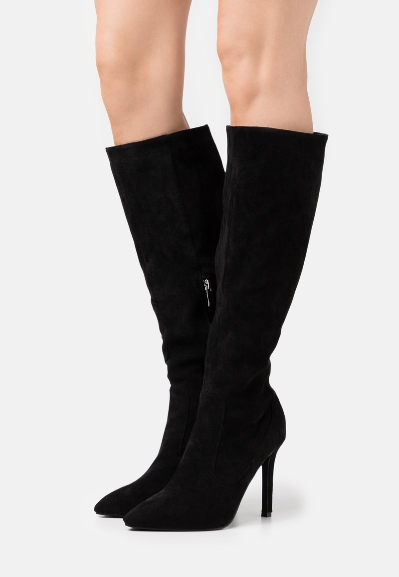 Botas negras por encima de la rodilla hechas de ante, con punta afilada, tacón stiletto alto y detalle de cremallera lateral. Textura suave y diseño elegante.