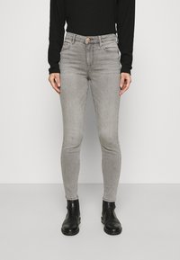 Jeans ajustados grises de cintura alta, con dos bolsillos frontales y cierre de botón. Se llevan con botas negras hasta el tobillo y una camiseta negra de mangas largas.
