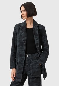 Blazer nero con motivo camouflage, dal taglio sartoriale, dotato di due tasche frontali e colletto a revers, realizzato in tessuto testurizzato.