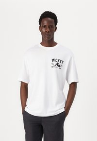 White cotton t-shirt featuring a black printed graphic stating "MICKEY" with accents and a round neckline. Short sleeves and relaxed fit.