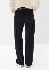 Dark navy corduroy pants with a straight leg design, featuring back pockets and a smooth black waistband. White rubber-soled shoes visible.