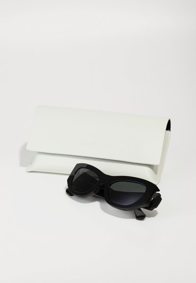 Óculos de sol pretos com armação angular e lentes escuras ao lado de uma caixa de couro branca em relevo com a inscrição "BURBERRY."