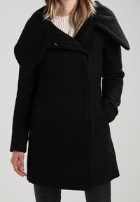 Black wool coat with a textured finish, oversized collar, zip closure, and side pockets. Features a fitted shape and below-hip length.