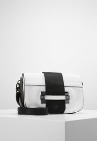 Bolso cruzado de cuero blanco y negro con acabado texturizado, forma rectangular, una correa central y acentos metálicos. Logo grabado en la parte delantera.