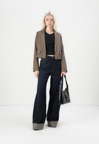 Brun cropped blazer, svart skjorte med knapper, mørke vid benjeans med brettede opplegg, og en svart skulderveske. Glatte teksturer og rene linjer.