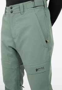 Groene outdoorbroek van een gladde, lichte stof, met knoopsluiting, meerdere zakken en logo-opdruk op de dij.