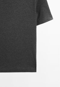 T-shirt en coton gris foncé à manches courtes vu de dos, avec un focus sur la moitié inférieure et la manche sur fond blanc.