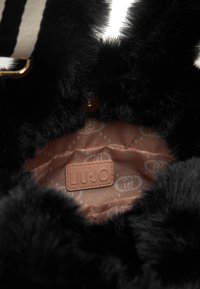 Borsa in eco-pelliccia nera con interno foderato in tonalità beige, caratterizzato da un motivo sottile. Include un'etichetta con il logo "LIU·JO" in rilievo.