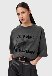 Maglietta oversized grigia scura realizzata in tessuto morbido, con una stampa grafica che presenta testo e un design di scheletro sul davanti.