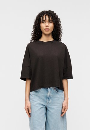 Czarny krótki t-shirt z miękkiej, lekkiej tkaniny, z szerokimi, krótkimi rękawami i okrągłym dekoltem, zestawiony z jasnoniebieskimi, luźnymi dżinsami.