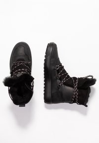 Bottes noires à la cheville en cuir texturé, doublure en fausse fourrure et lacets à motifs. Semelle en caoutchouc épaisse avec une bande de roulement prononcée pour une meilleure adhérence.