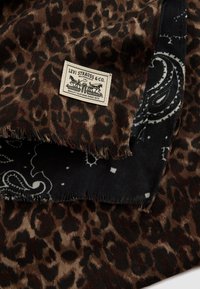 Luipaardprint stof met rafelige randen, voorzien van een contrasterende zwart paisley-patroon strook en een Levi Strauss-gekleurd label.