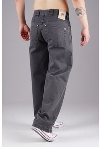 Gray denim jeans with a relaxed fit, featuring a branded patch on the back, buttoned pockets, and contrasting stitching details.
