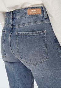 Světle modré džíny z denimu s texturovaným povrchem, s hnědou koženou značkovou nášivkou, zadními kapsami a klasickým pěti-kapsovým střihem.