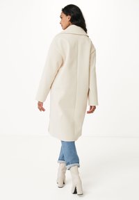 Beige, mid-lång kappa med bred krage, sänkt axlar och sidofickor, tillsammans med blå jeans med uppvikta ärmar och beige klackstövlar.