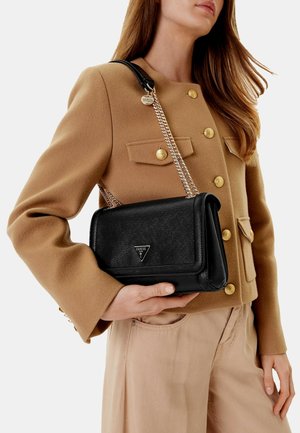 Borsa nera con texture, dotata di un logo triangolare e una tracolla a catena, abbinata a un giubbotto color cammello con bottoni dorati.