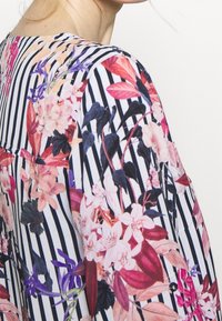 Tkanina w kwiatowy wzór z mieszanką różu, fioletu i zieleni na białym i granatowym tle w paski, charakteryzująca się miękką fakturą i luźnym krojem.