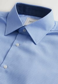 Camicia azzurro chiaro in tessuto stampato, con colletto classico, chiusura con bottoni e dettaglio del colletto interno di un blu scuro a contrasto.