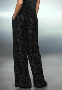 Pantaloni negri cu talie înaltă, confecționați dintr-un material texturat, având un model floral discret și buzunare laterale. Design lejer, cu picioare late.